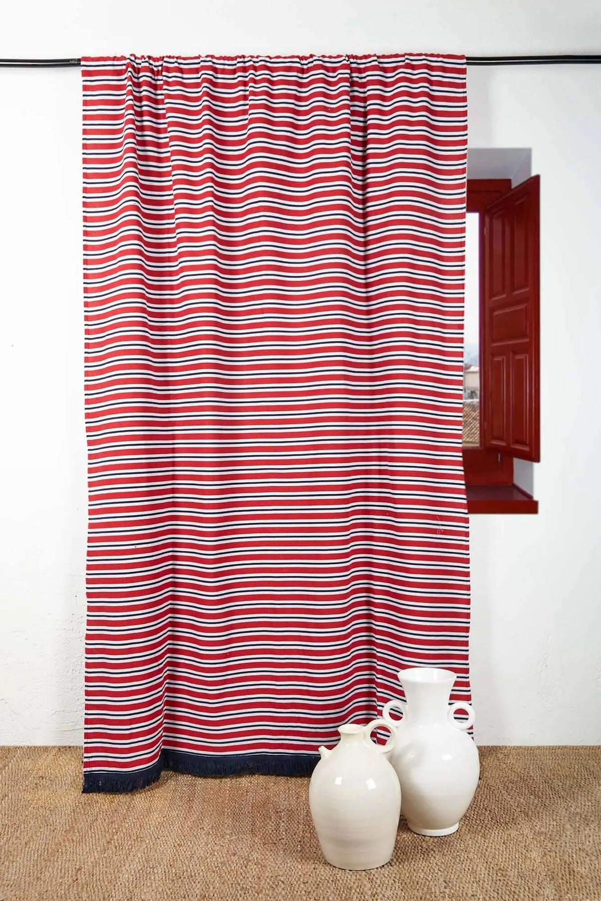 Cortina de loneta con rayas horizontales rojas, blancas y azul marino, con flecos inferiores y estilo mediterráneo.