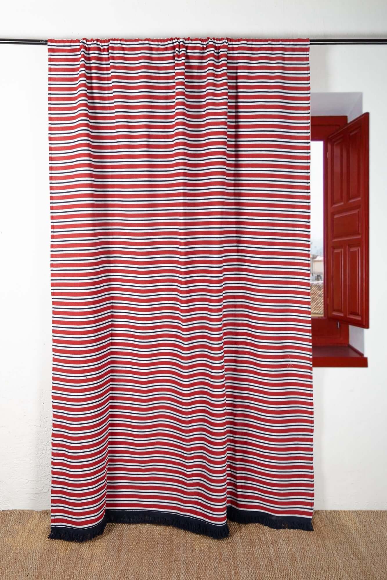 Red, white, and navy blue striped canvas curtain hanging from a rod, featuring a tasseled hem.