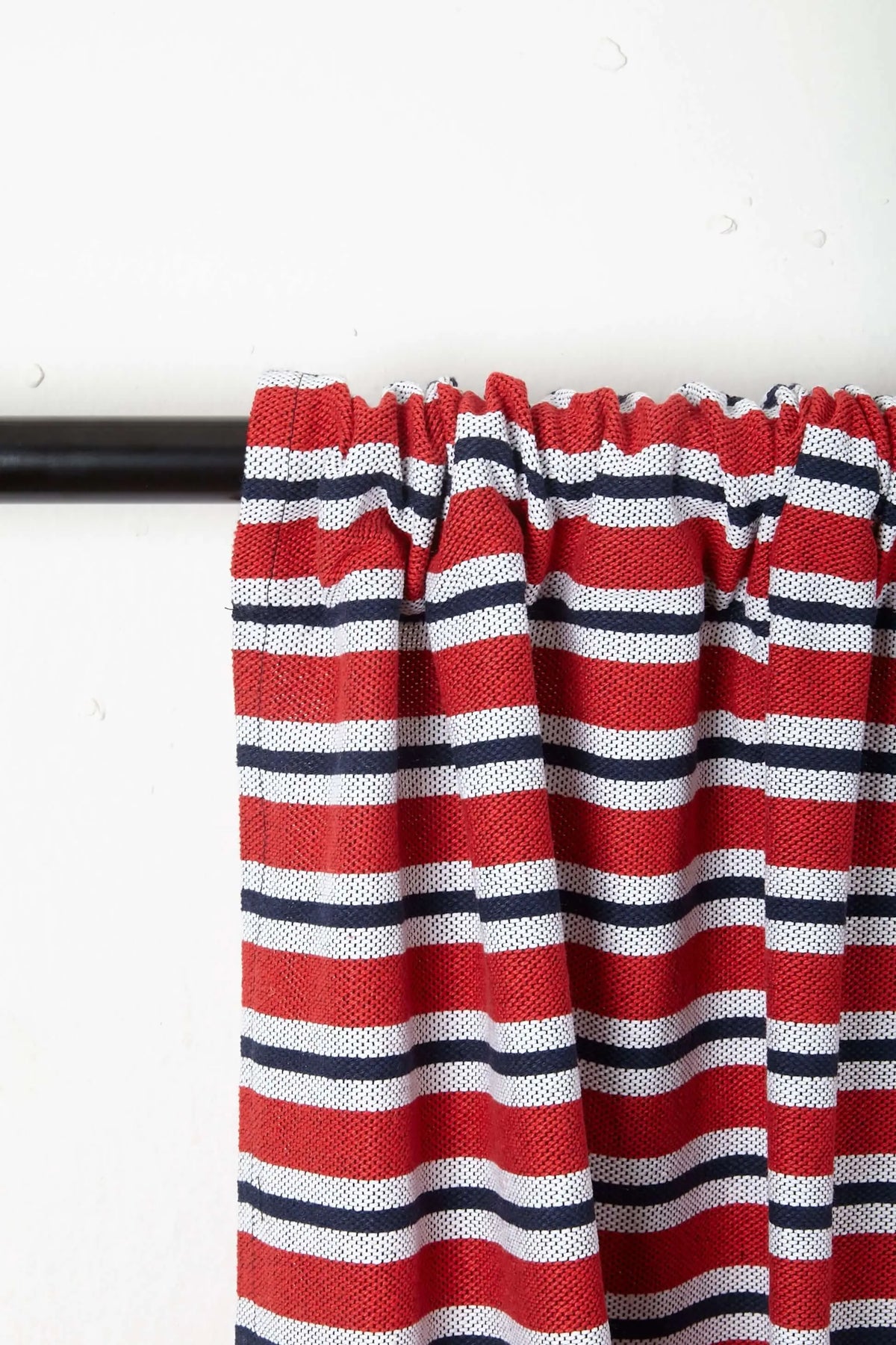 Cortina de loneta con diseño de rayas horizontales en rojo, azul marino y blanco, colgada en una barra negra.