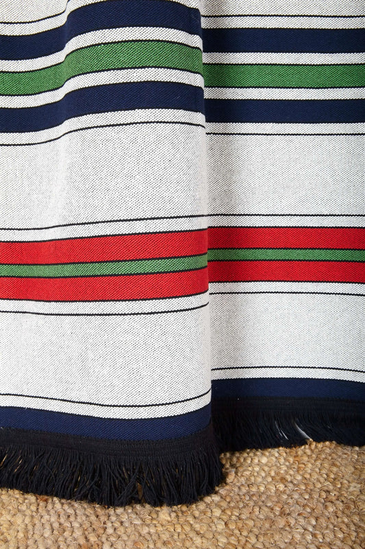 Cortina de tejido canario con rayas horizontales en azul, rojo, verde y blanco, terminada con flecos negros decorativos.