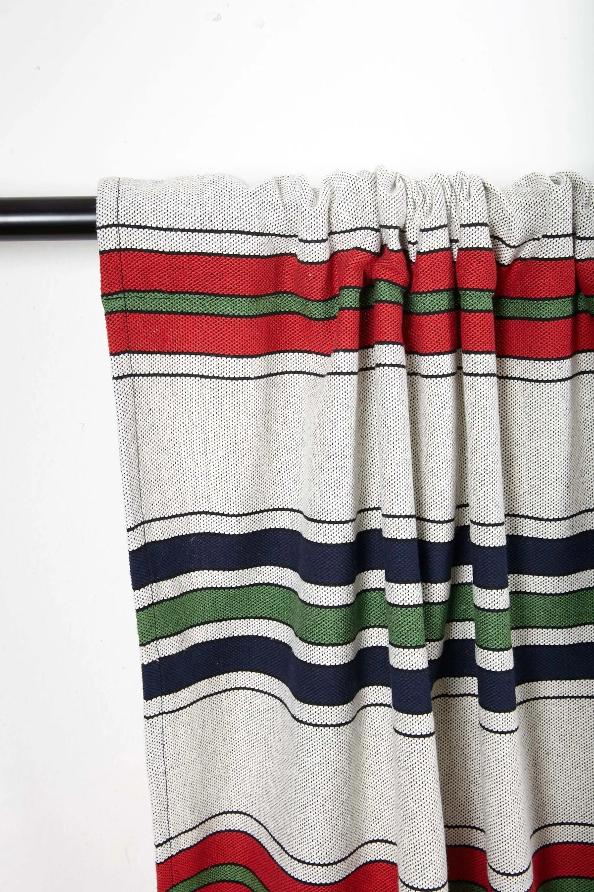 Textured off-white curtain with horizontal stripes in red, navy blue, and green hanging on a black rod.