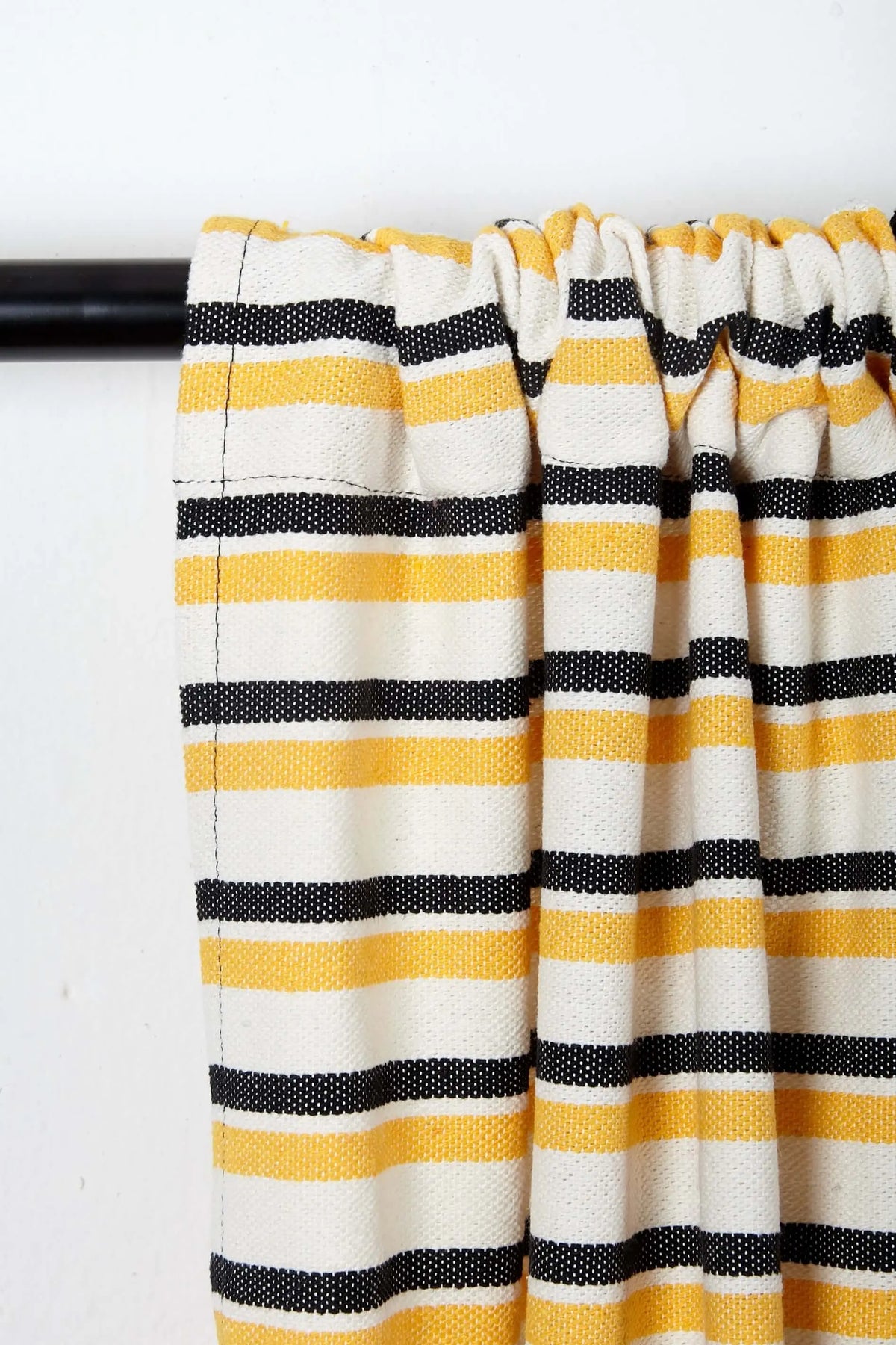 Canvas curtain featuring horizontal stripes in yellow, black, and cream, hanging on a black rod.
