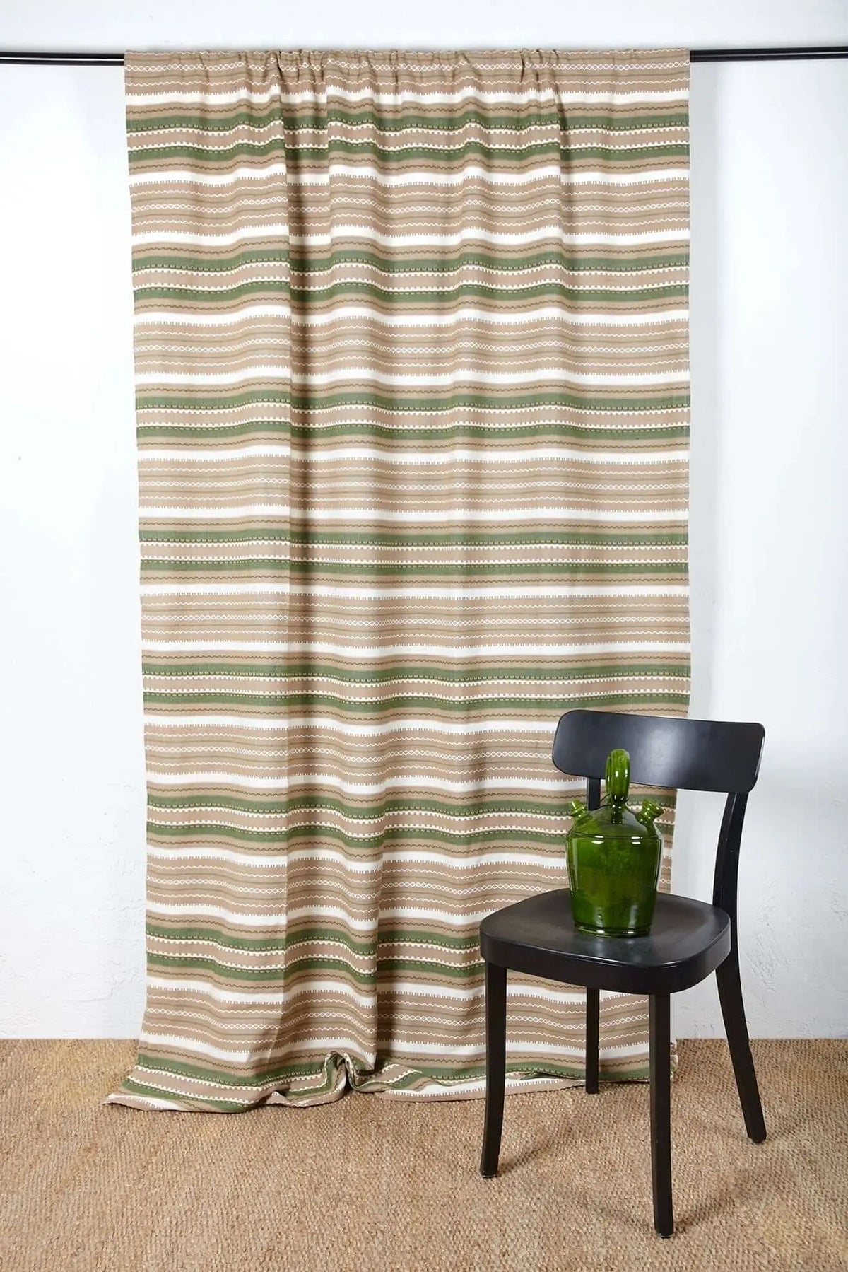 Artisanal curtain with horizontal striped pattern in green, brown, and white, hanging on a rod behind a black chair.