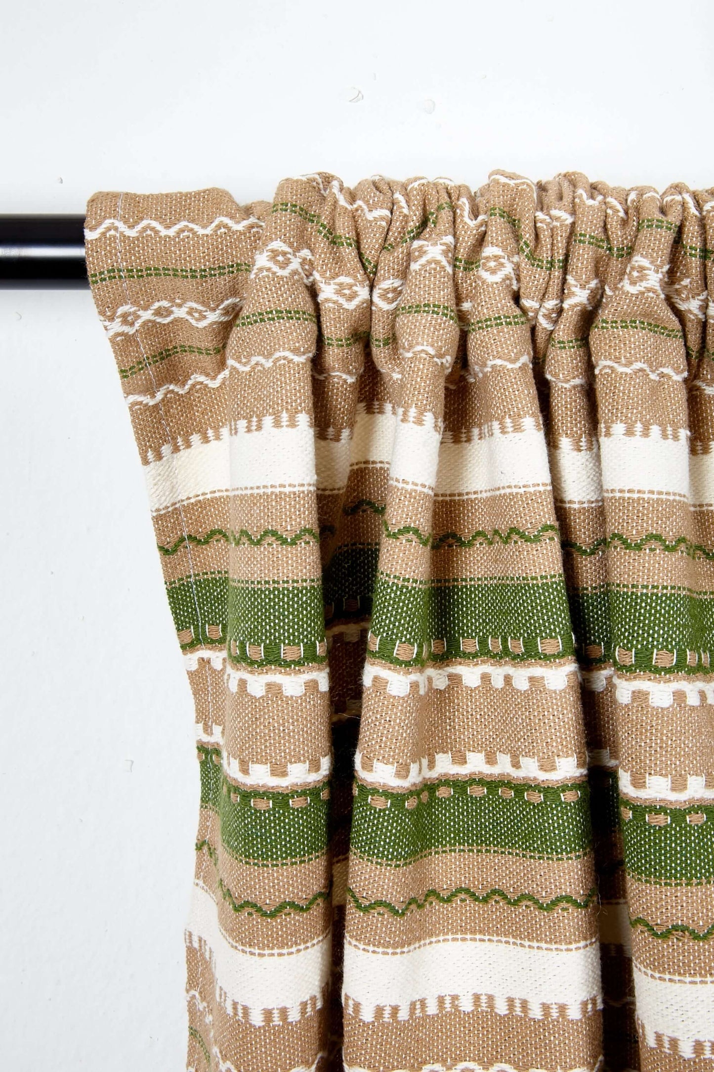 Artisanal curtain with brown, green, and cream striped pattern and geometric textured weave on a curtain rod.