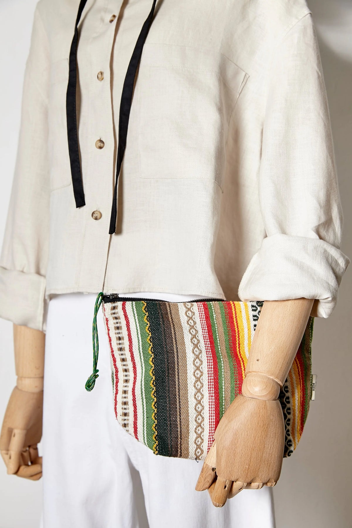 Neceser de tela con estampado de rayas verticales multicolores y textura artesanal, cerrado con cremallera y cordón.