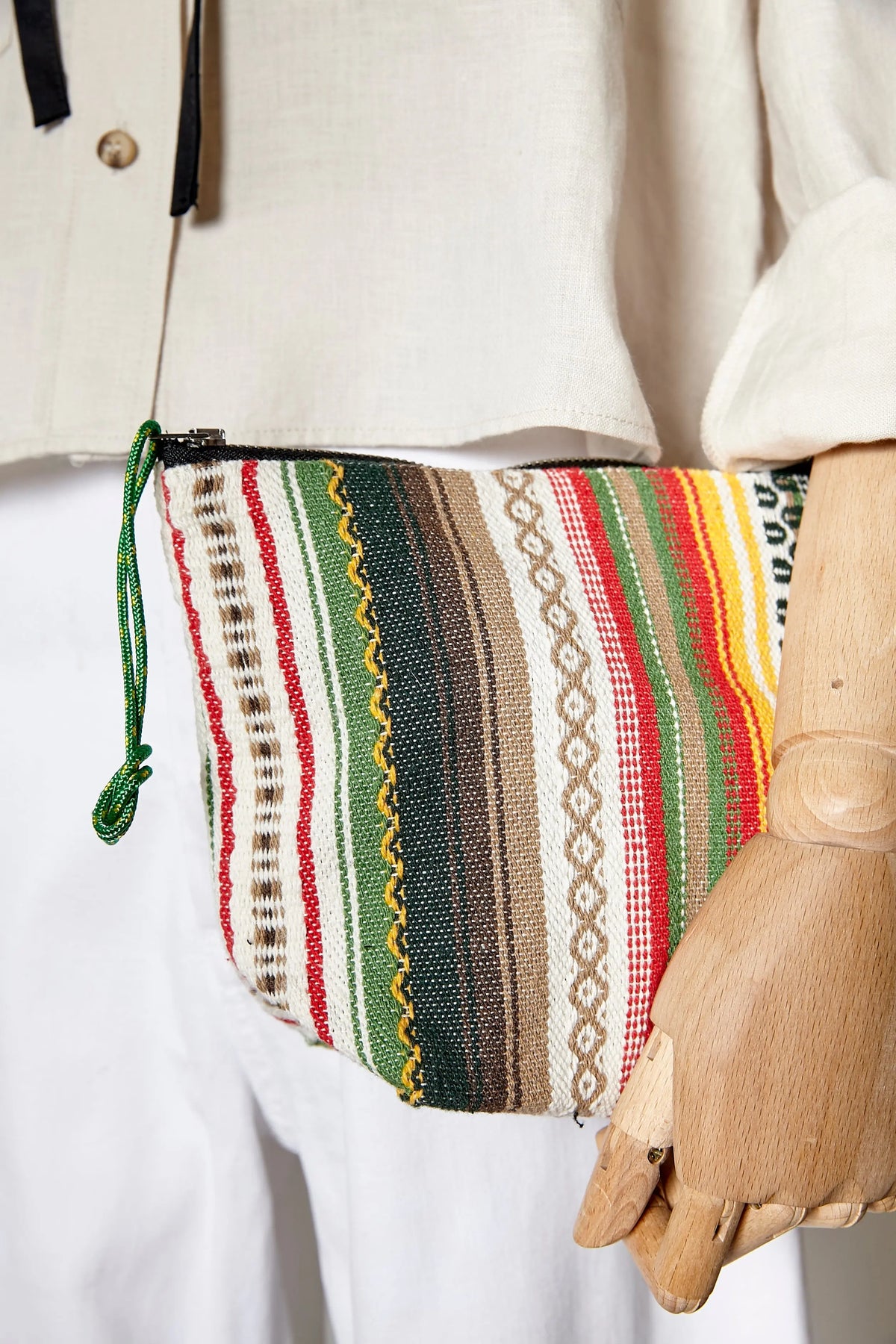 Neceser de tela artesanal con rayas multicolores, estilo alpujarra, cierre de cremallera y tirador de cordón verde.