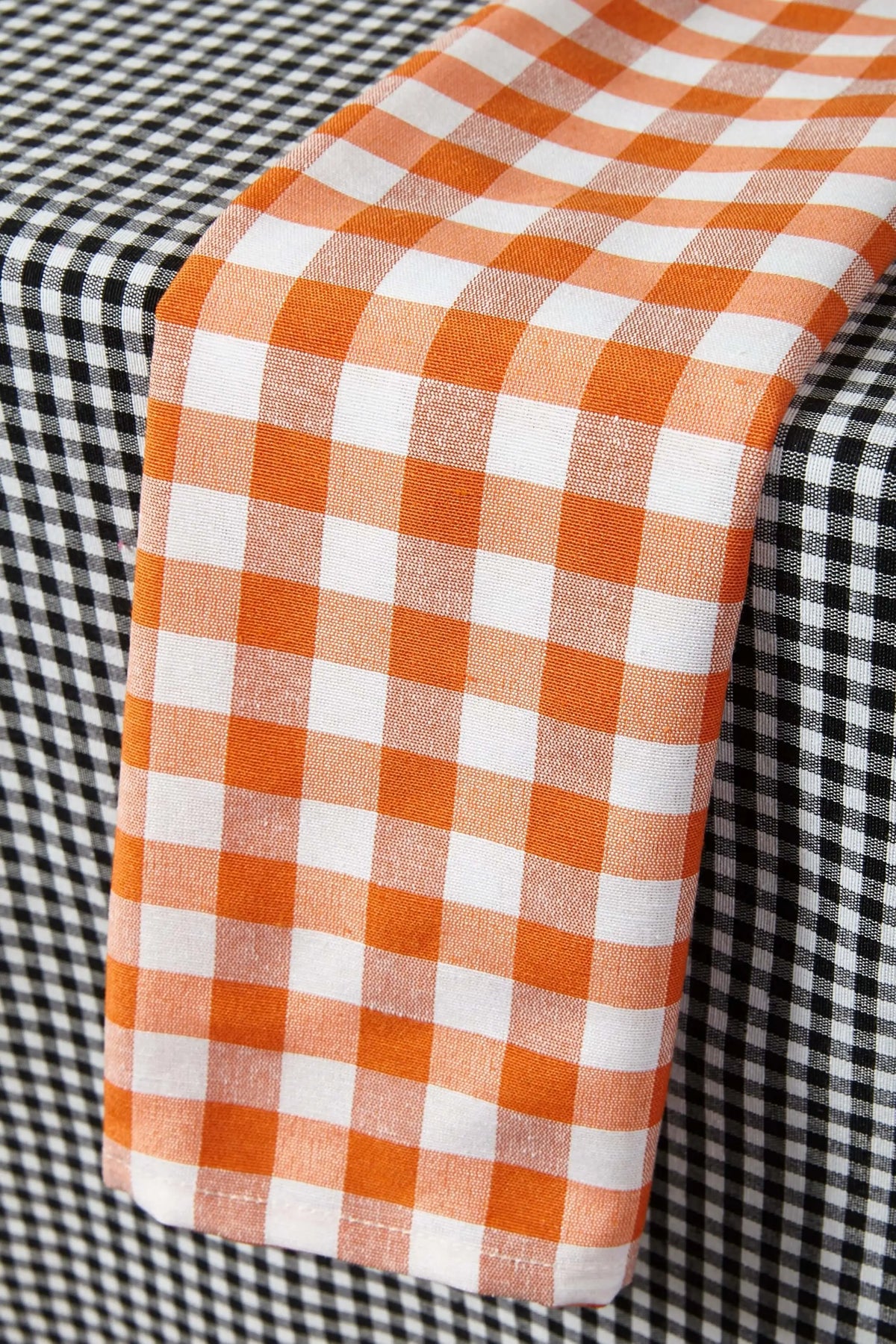 Mantel de tela con estampado de cuadros vichy. Muestra dos colores: negro y naranja combinados con blanco.