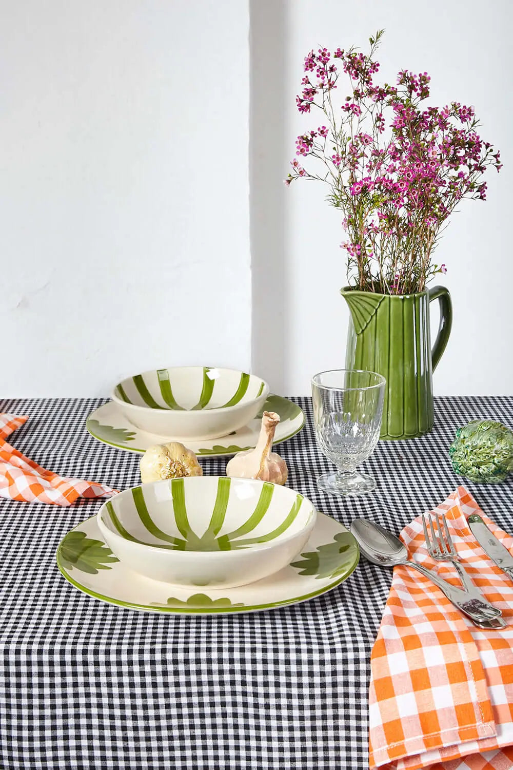 Mantel de tela con estampado de cuadros vichy en color negro sobre una mesa con vajilla y flores.