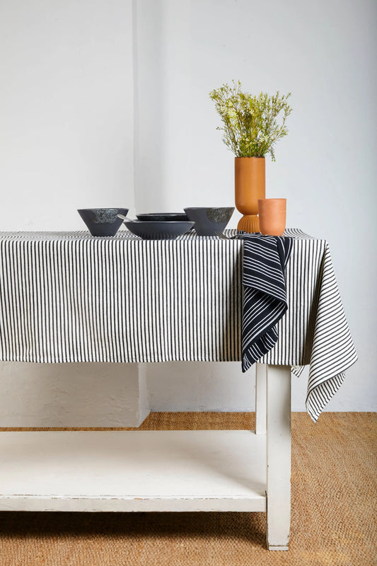 Black and white striped cotton canvas tablecloth on a table with modern stoneware bowls and terracotta vases.