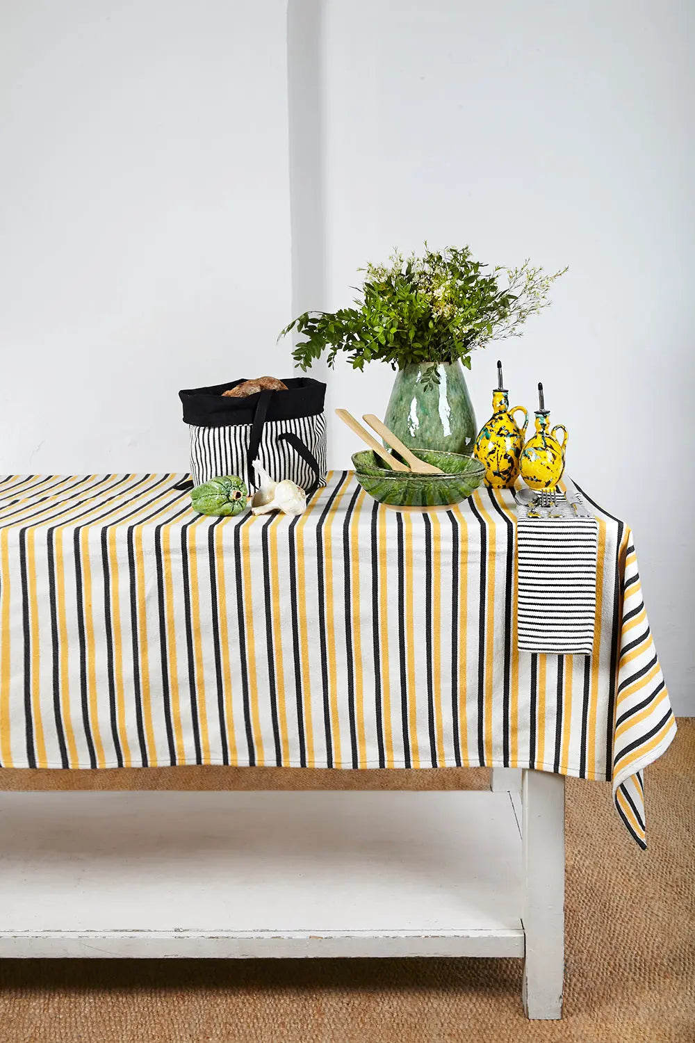 Mantel de loneta con diseño de rayas verticales en amarillo, negro y blanco sobre mesa decorada con menaje rústico.