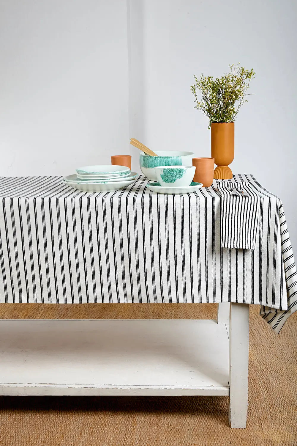 Black and white striped cotton tablecloth draped over a table, set with speckled dishes and a vase.