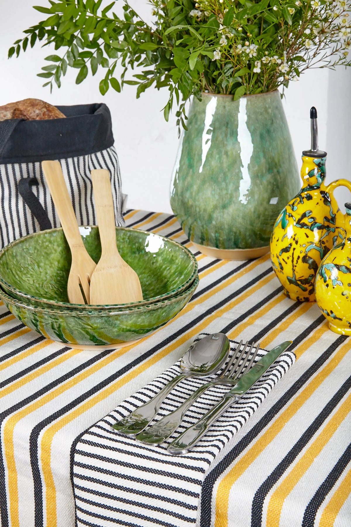 Mantel de loneta con diseño de rayas verticales en amarillo, negro y blanco, sobre una mesa con vajilla y decoración.
