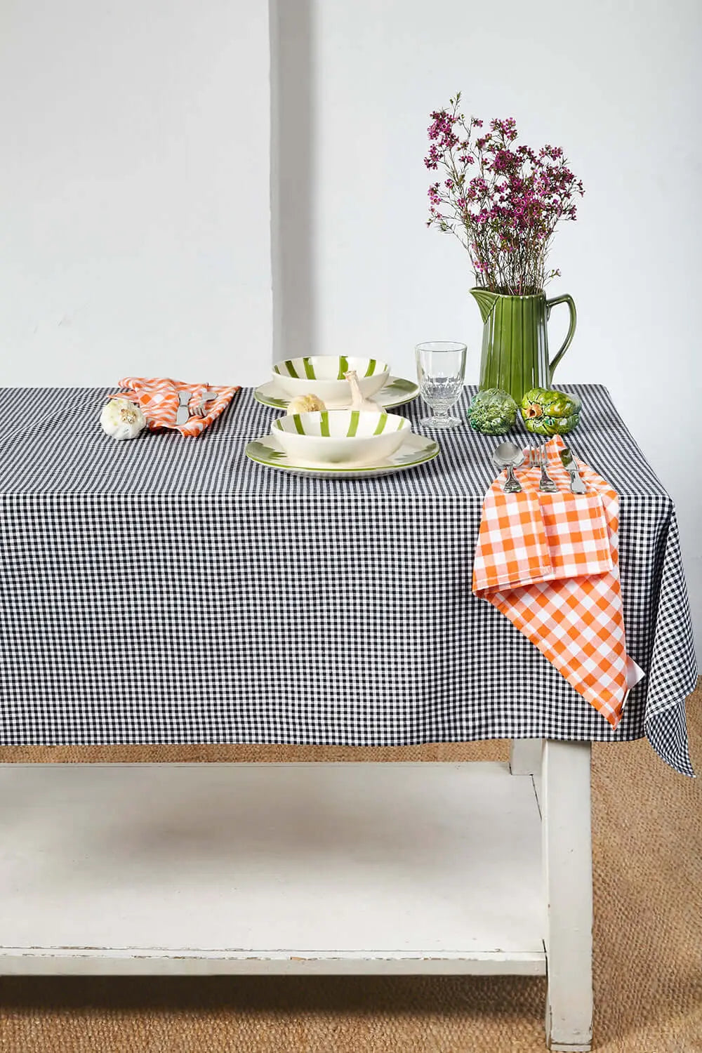 Mantel de tela con estampado de cuadros vichy en blanco y negro, sobre una mesa con vajilla y servilletas naranjas.