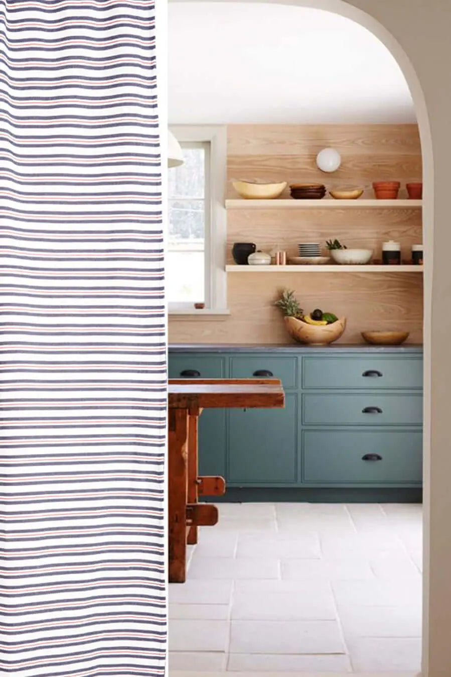 Cortina de loneta con estampado de finas rayas azules y rojas, estilo casual, junto a una cocina rústica.