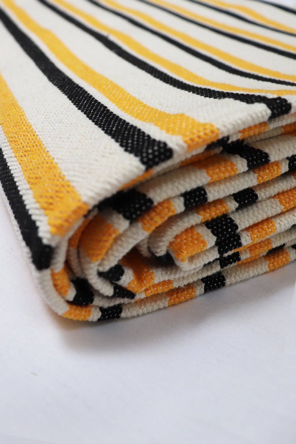 Folded canvas tablecloth with a textured weave, featuring bold vertical stripes in black and vibrant yellow.