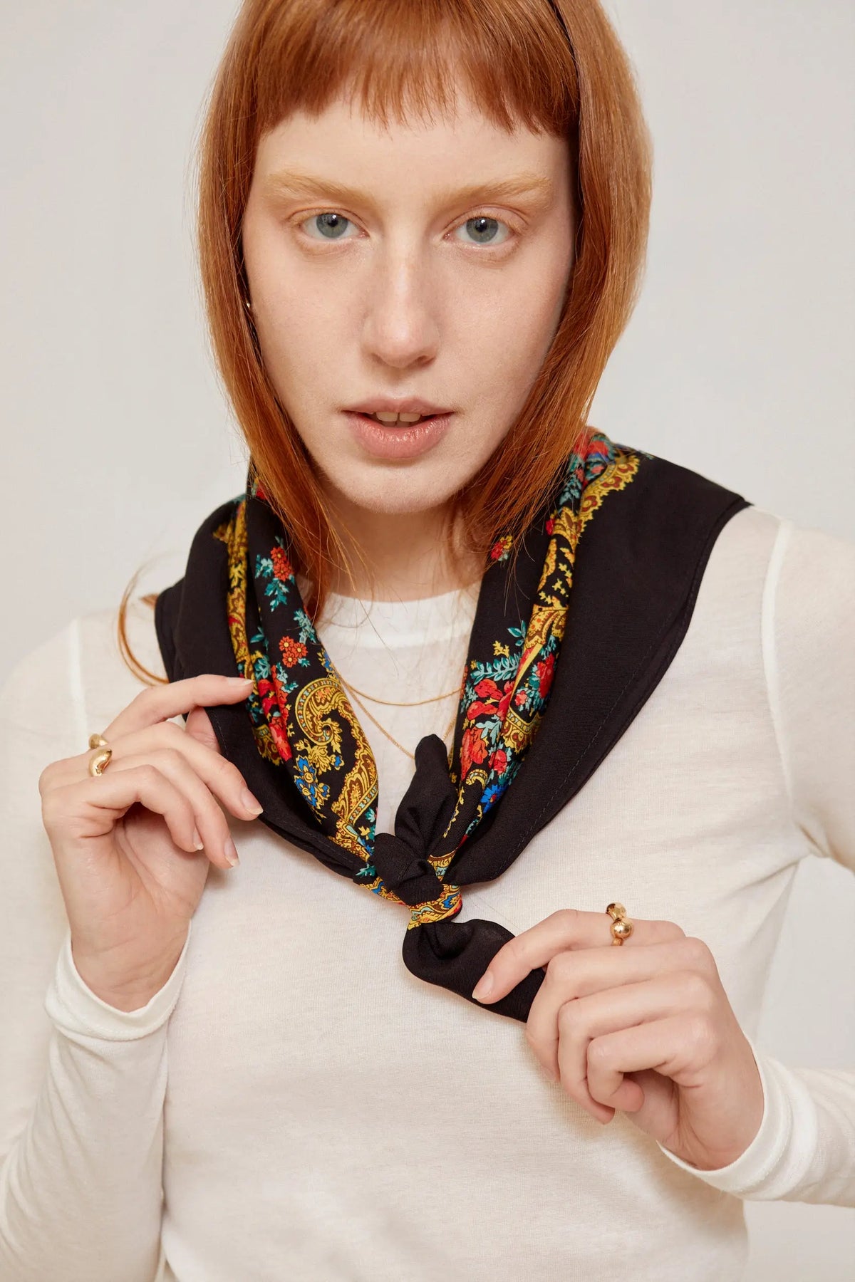 Black scarf featuring an ornate gold chain and vibrant floral border pattern, tied elegantly around the neck.