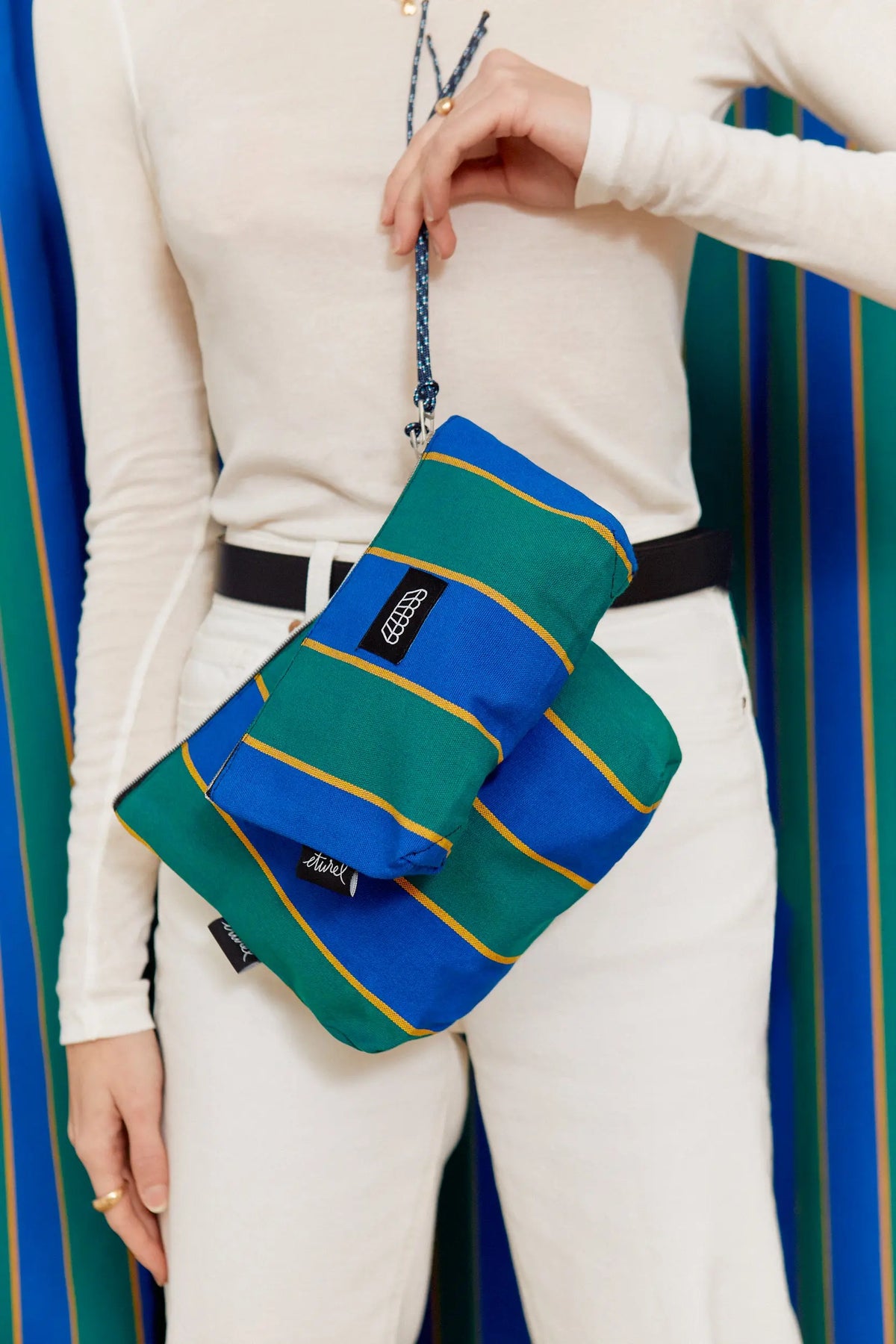 Canvas toiletry bag and matching pencil case in blue and green stripes with a blue rope handle held by a person.