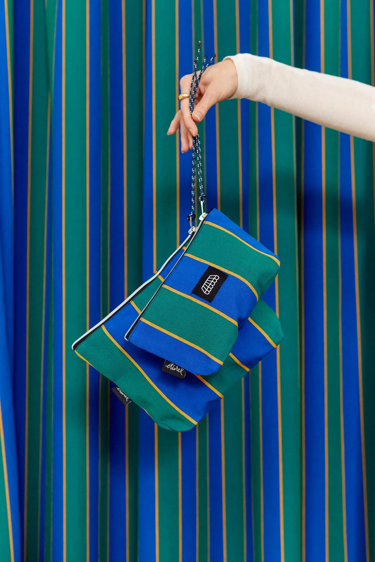 Handheld rectangular toiletry bag in blue, green, and yellow striped canvas with a matching rope carry cord.