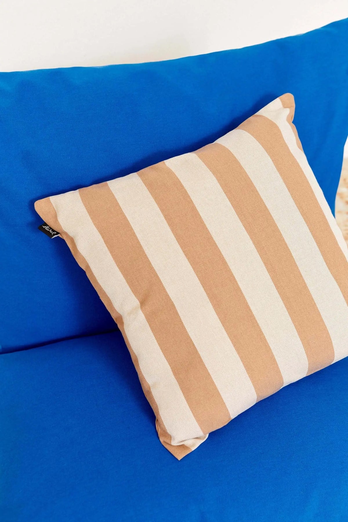 Funda de cojín cuadrada de 50x50cm en lona resistente con rayas verticales en tonos beige sobre fondo azul intenso.