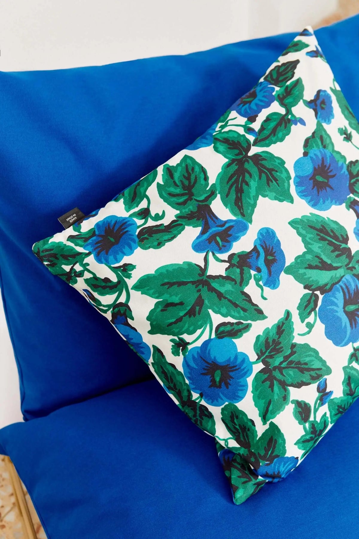 Funda de cojín de 50x50 cm en lona con estampado floral de flores azules y hojas verdes sobre fondo blanco.