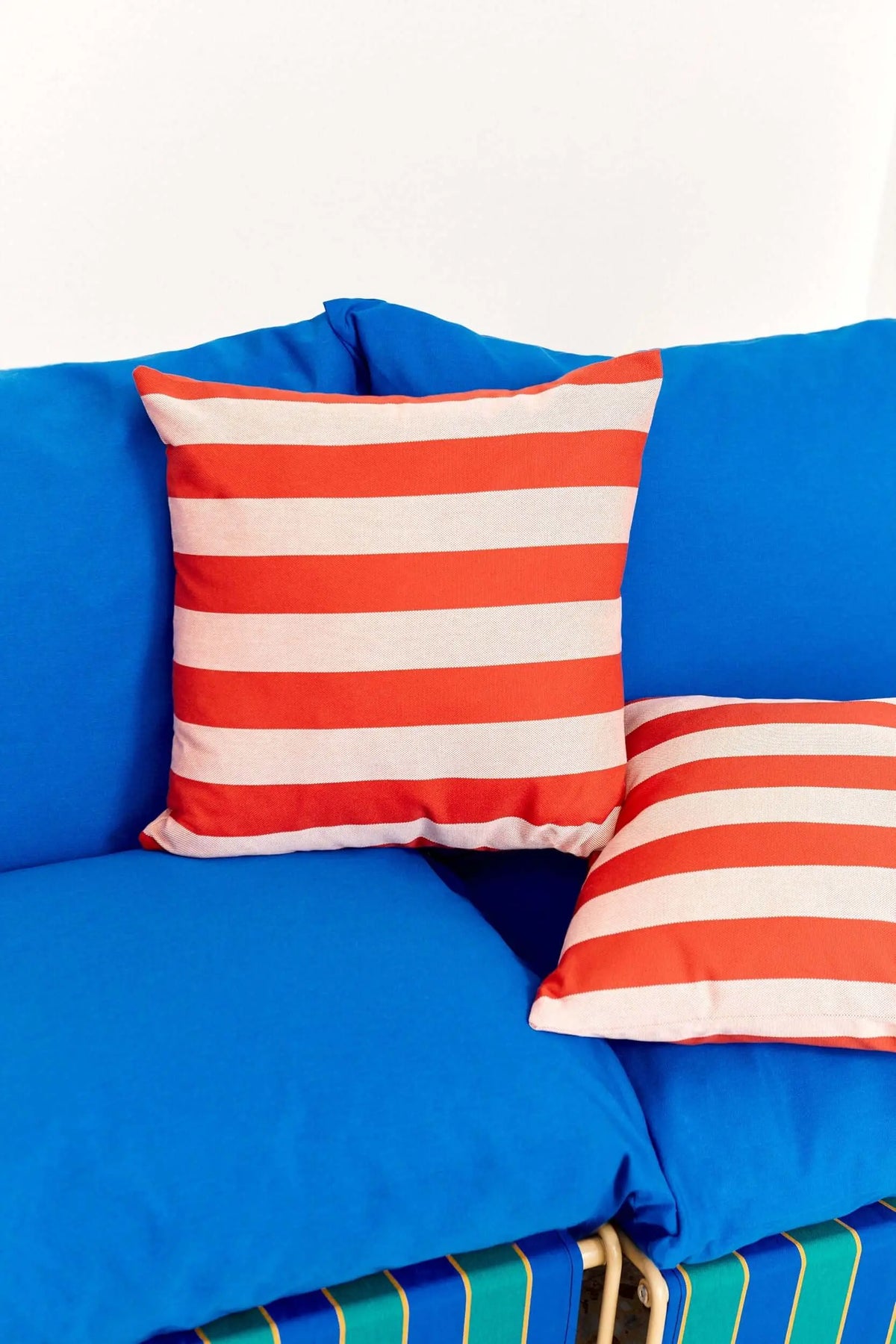 Square cushion covers in red and white horizontal stripes made of sturdy awning canvas, placed on a blue sofa.