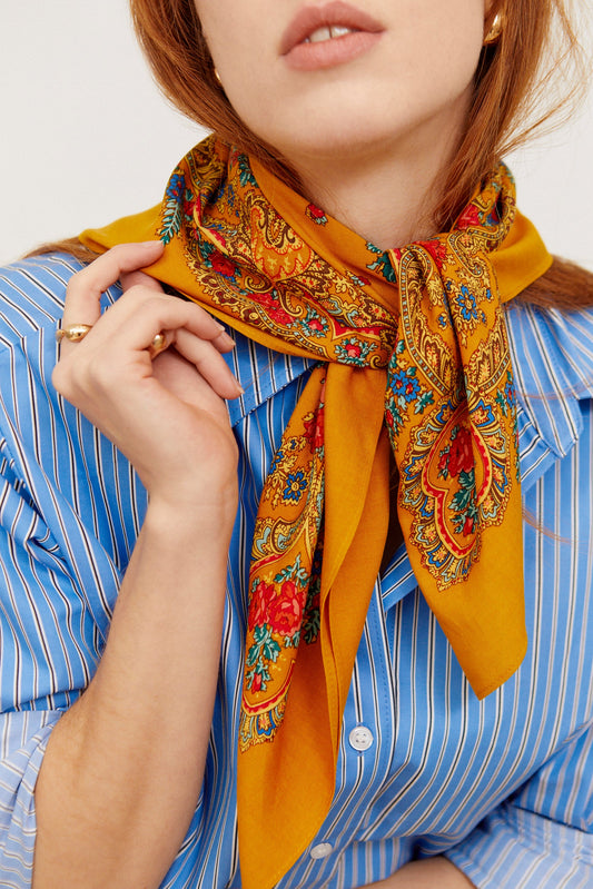 Pañuelo de seda ocre con estampado floral y geométrico multicolor, estilo tradicional portugués, anudado al cuello.