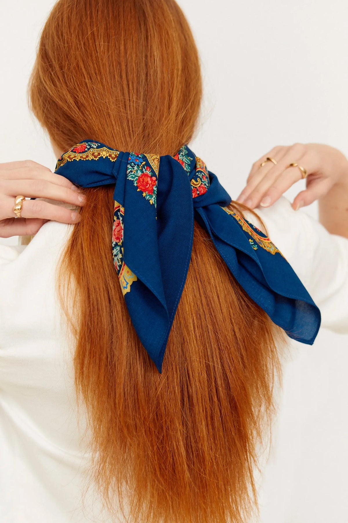 Pañuelo azul marino con estampado floral estilo portugués anudado en el cabello de una mujer pelirroja.