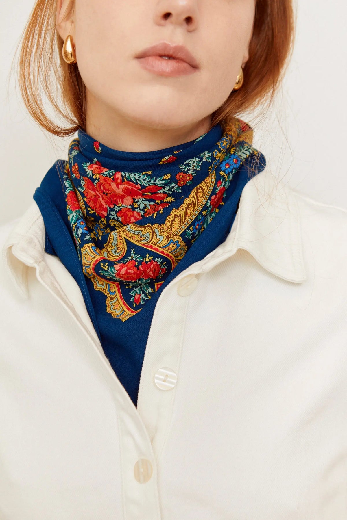 Navy blue scarf with a vibrant red floral and yellow chain pattern, tied around a woman's neck under a white shirt.