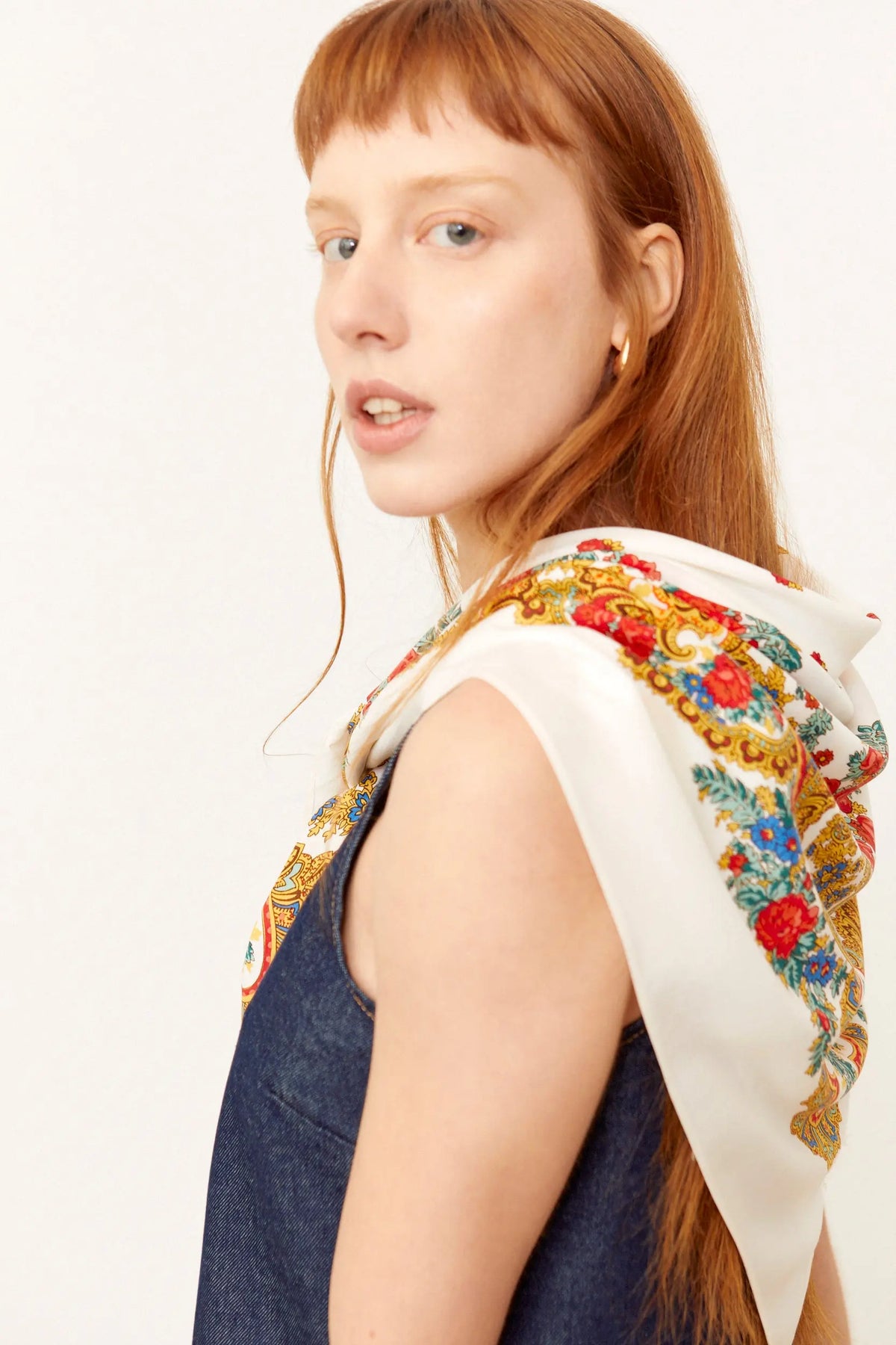 Pañuelo blanco con estampado de cadenas y flores rojas y azules sobre los hombros de una mujer de cabello pelirrojo.