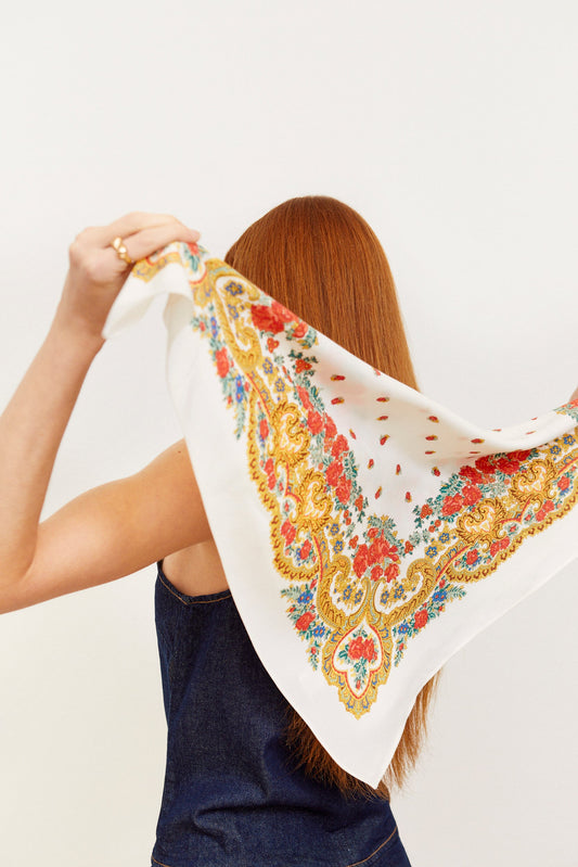 Pañuelo blanco con estampado de flores rojas, detalles en dorado y motivos de cadenas estilo clásico sobre fondo claro.