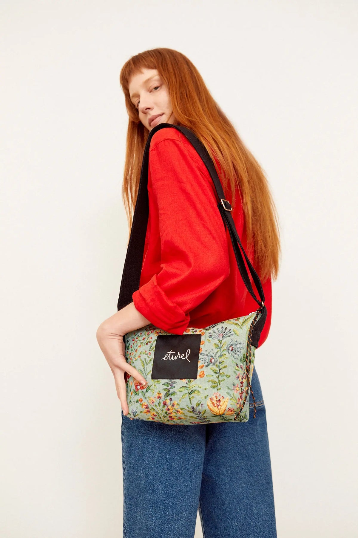Bolso bandolera de tejido jacquard en tono celeste con estampado de azaleas coloridas y correa negra ajustable.