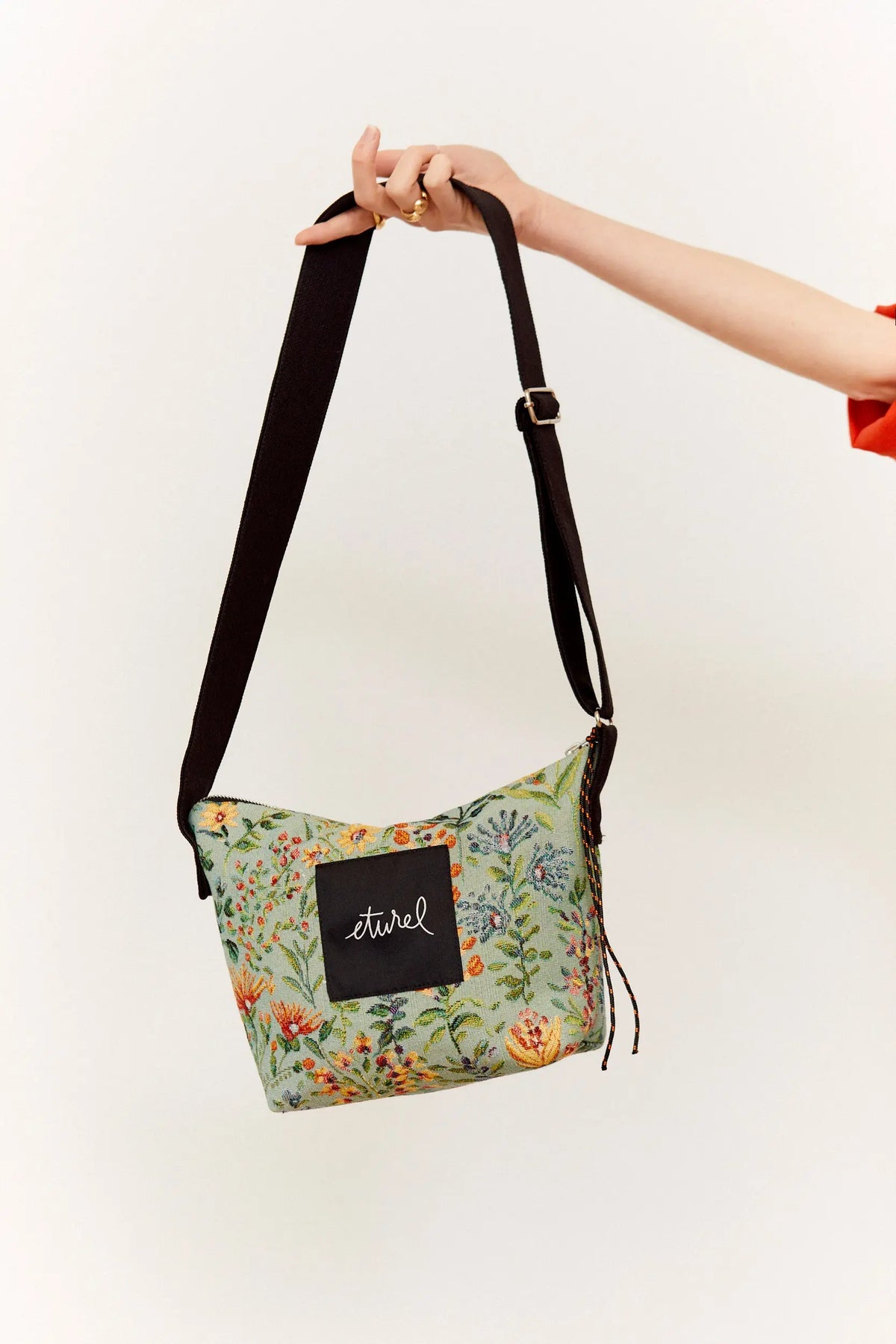 Bolso bandolera de tejido jacquard con estampado floral en tonos celestes y correa negra ajustable.