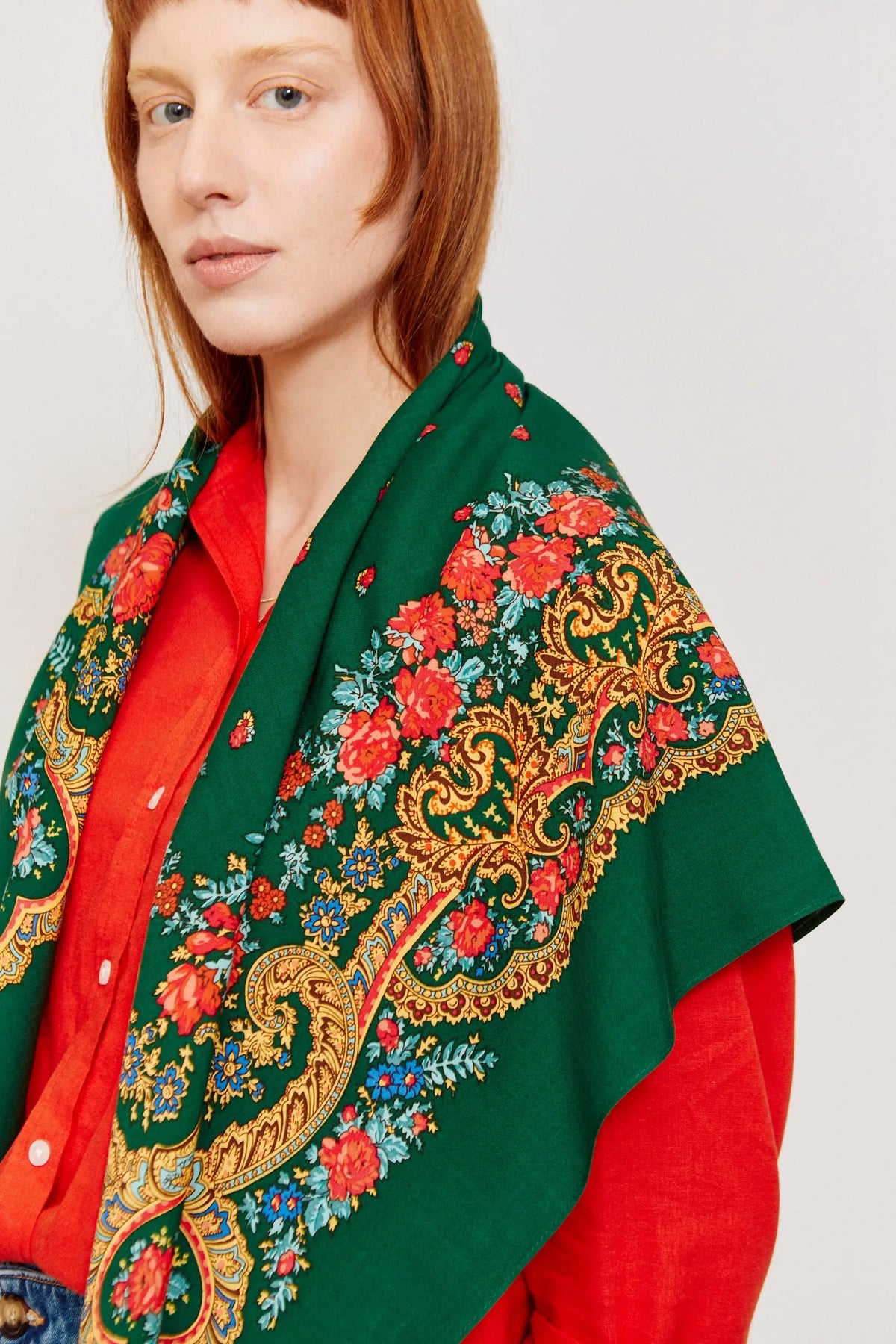 Pañuelo verde botella con estampado floral tradicional y motivos de cadenas doradas sobre hombros de una mujer.