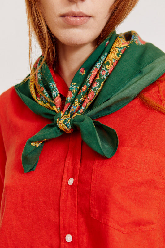 Pañuelo verde botella con estampado floral y cadenas anudado al cuello, estilo tradicional portugués sobre camisa roja.