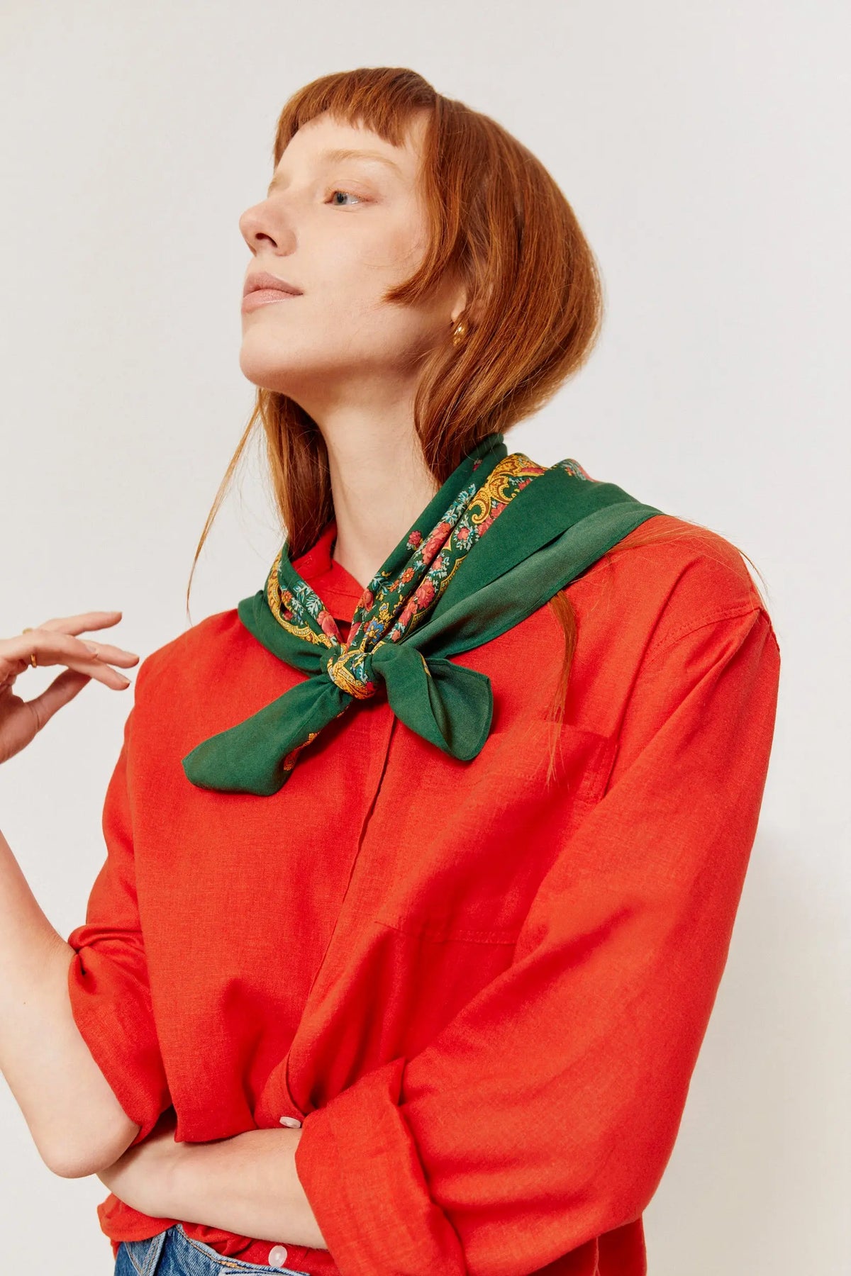 Pañuelo verde botella con estampado de cadenas y flores anudado al cuello de una modelo con camisa roja.