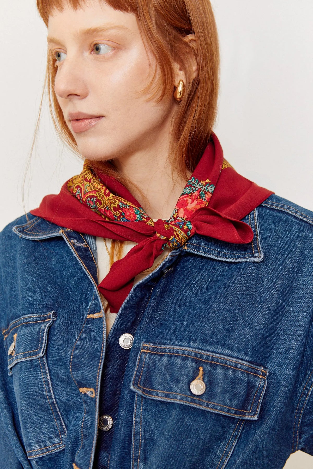 Pañuelo granate con estampado floral y cadenas, anudado al cuello, sobre una mujer con chaqueta vaquera.
