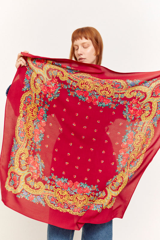 Pañuelo granate con estampado floral clásico y cenefa dorada estilo barroco, tejido ligero sobre mujer sosteniéndolo.