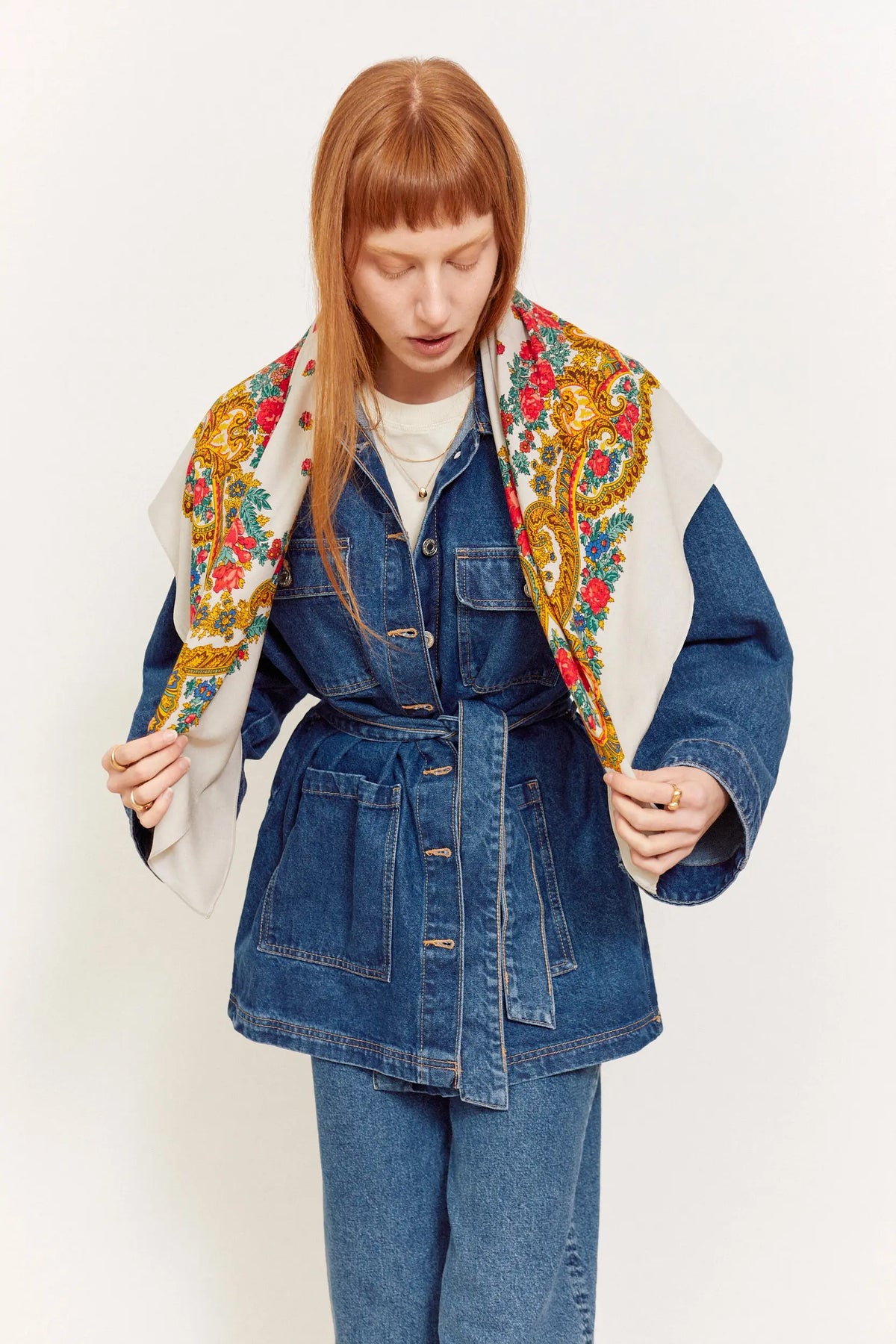 Pañuelo gris con estampado floral y de cadenas en tonos rojos y amarillos, usado sobre una chaqueta de mezclilla azul.
