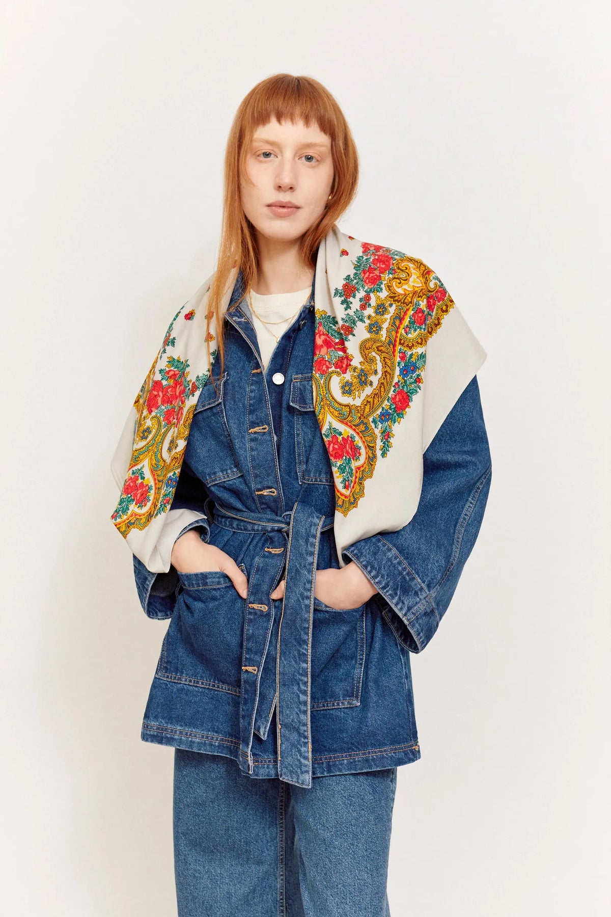 Grey Portuguese scarf with vibrant floral and gold chain-link patterns worn over a belted blue denim jacket.