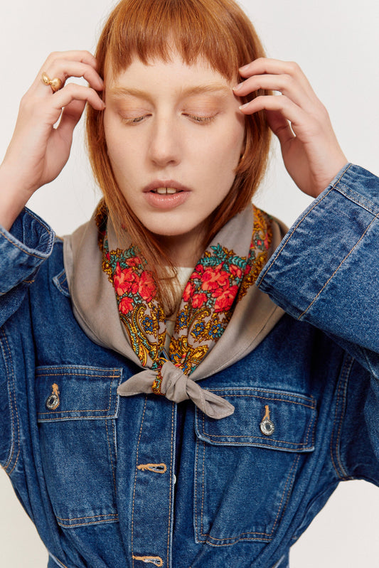 Pañuelo gris con estampado floral colorido, anudado al cuello sobre una chaqueta vaquera azul.