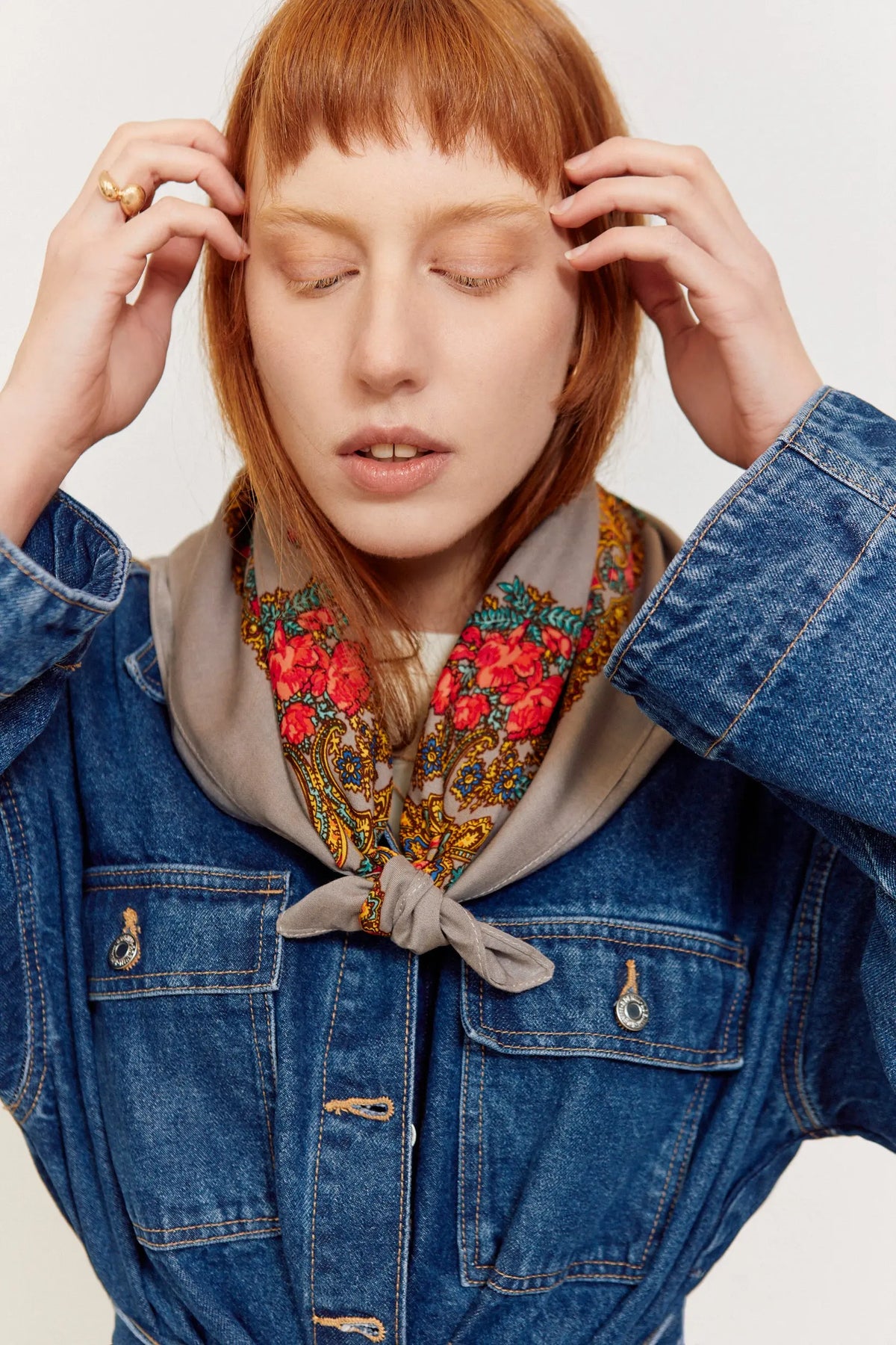 Pañuelo gris con estampado floral colorido, anudado al cuello sobre una chaqueta vaquera azul.
