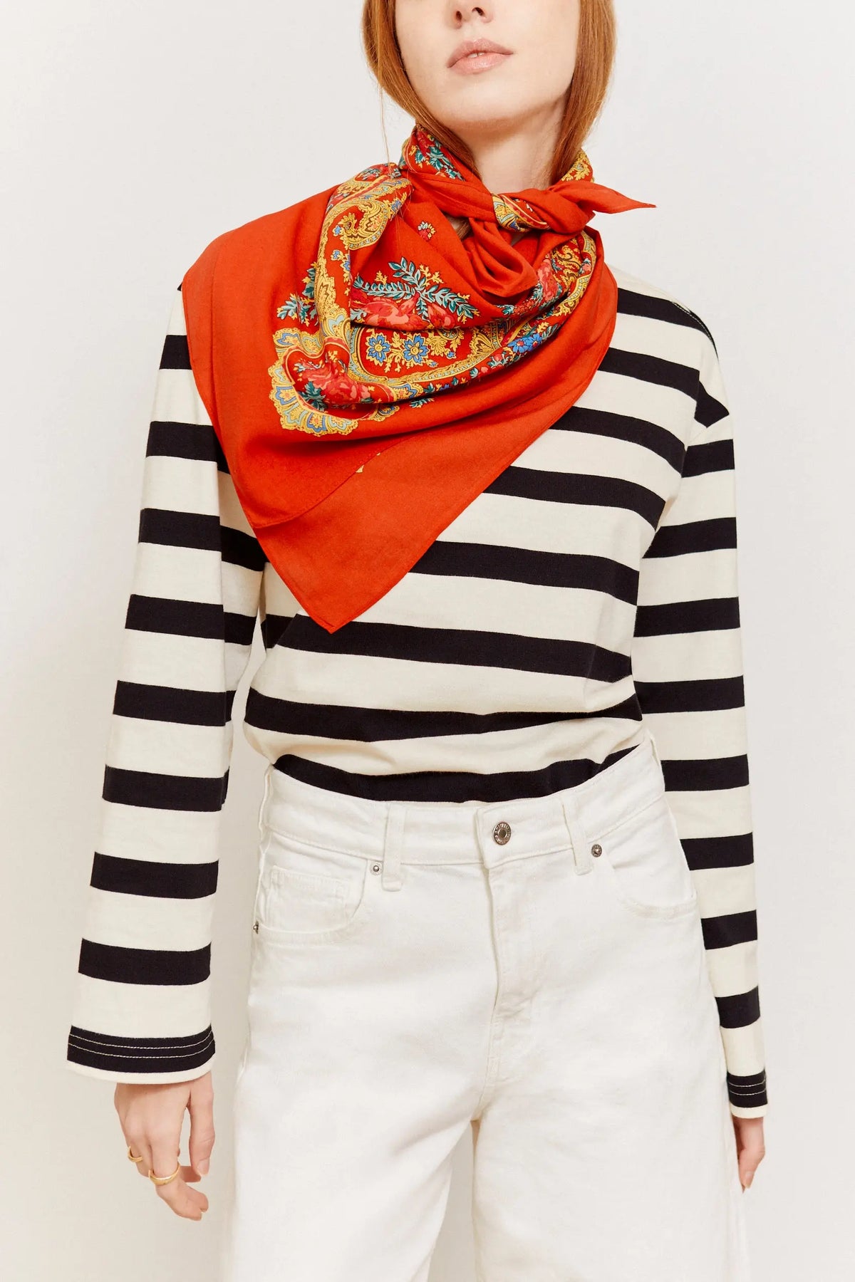 Pañuelo rojo con estampado de cadenas y motivos florales anudado al cuello sobre camiseta de rayas blancas y negras.