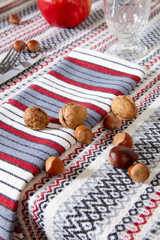 Woven tablecloth with red, grey, and black stripes and geometric patterns, displayed with walnuts and hazelnuts.