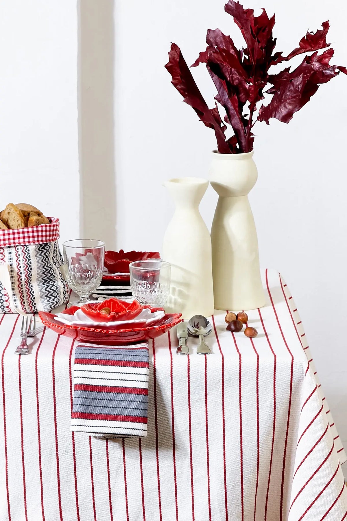 Mantel de loneta blanco con rayas verticales granates, presentado en una mesa decorada con vajilla y elementos naturales.