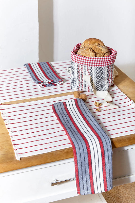 Two white canvas placemats with thin red stripes, featuring folded, multi-colored striped napkins and a bread basket.
