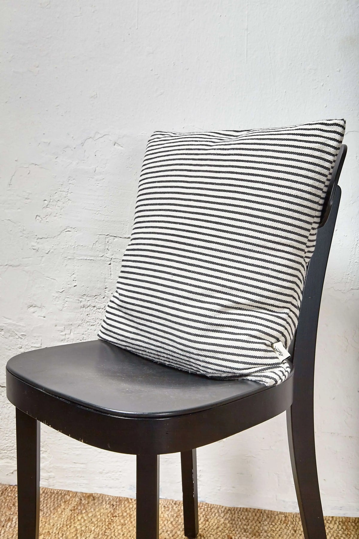 Cojín cuadrado de loneta con rayas horizontales blancas y negras, sobre una silla de madera oscura.