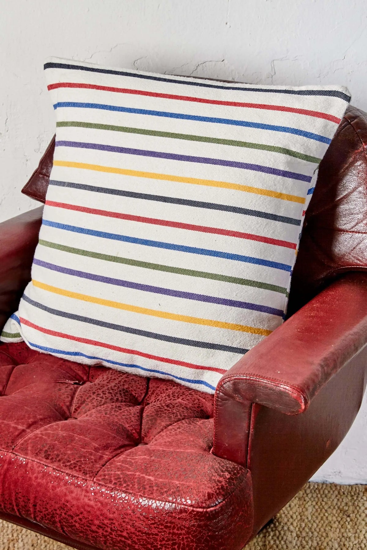 Square 50x50cm woven cushion with a multi-colored horizontal striped pattern on an off-white background.