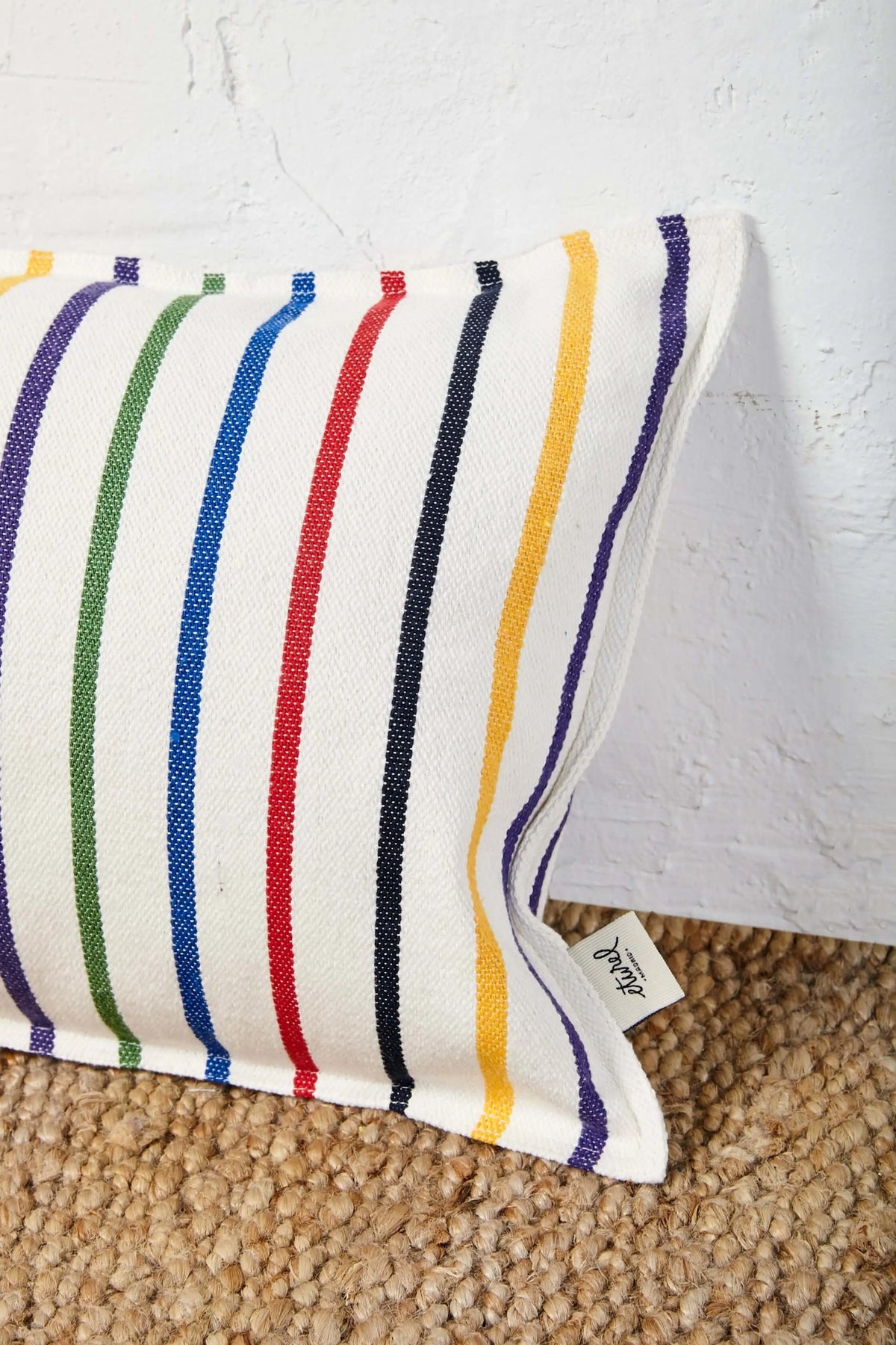 Rectangular cushion with a cream textured fabric and vertical stripes in blue, red, yellow, green, and dark navy.