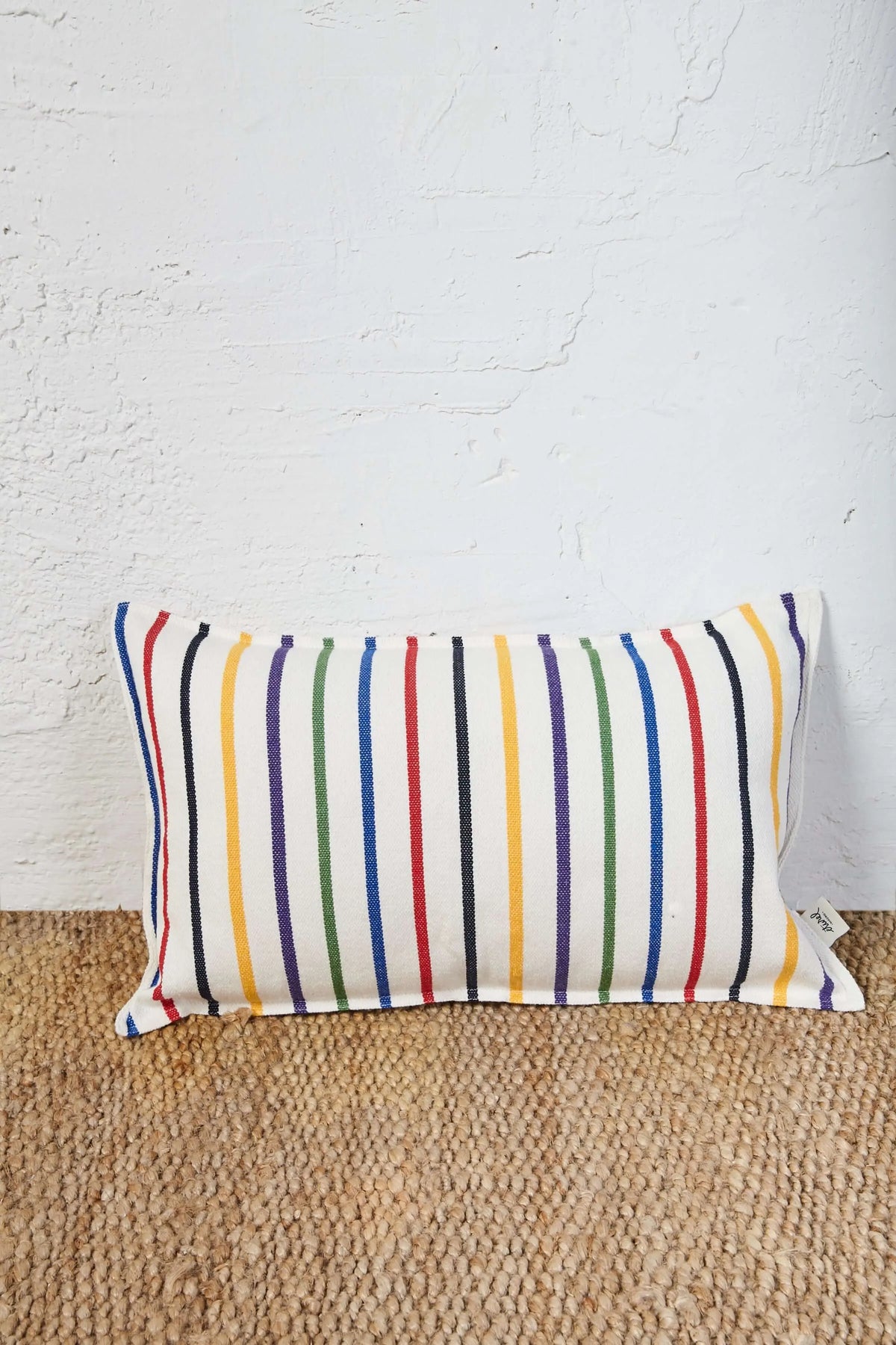 Rectangular cushion in off-white woven fabric with colorful vertical stripes of yellow, red, blue, green, and black.