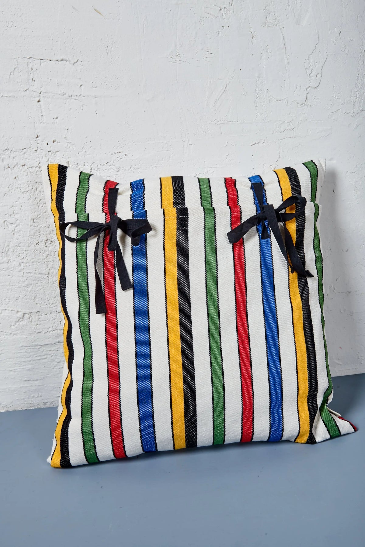 Cojín cuadrado de algodón con rayas multicolores y lazos negros, estilo moderno y vibrante.